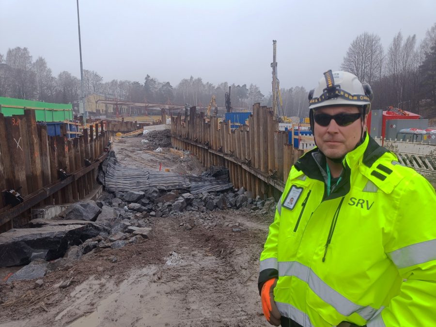 Työmaavaatteisiin ja -varusteisiin pukeutunut mies avolouhinta-alueen edessä.
