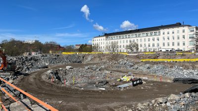 Työmaa-alueella kivikasoja ja ympyrän mallinen työmaatie. Taustalla iso valkoinen sairaalarakennus.